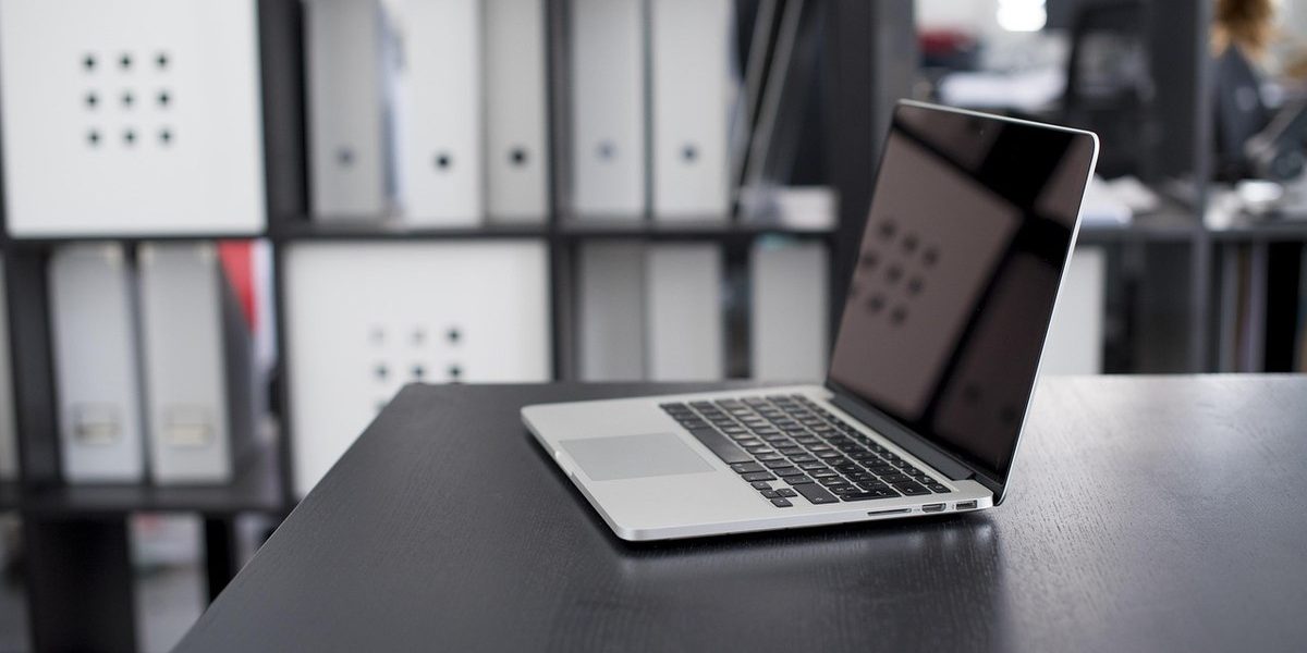 Ordinateur portable ouvert sur un bureau noir avec étagères de rangement en arrière-plan dans un bureau