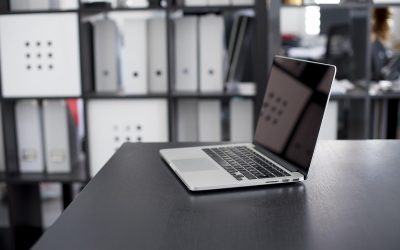 Ordinateur portable ouvert sur un bureau noir avec étagères de rangement en arrière-plan dans un bureau