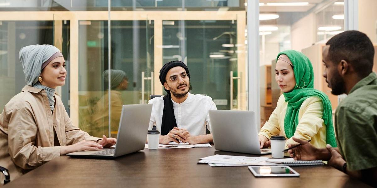Quatre collaborateurs en hijab et casquette discutent autour de leurs ordinateurs