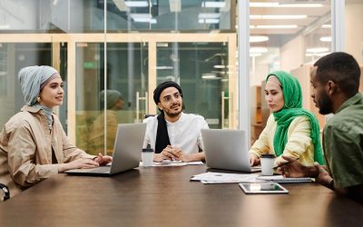 Quatre collaborateurs en hijab et casquette discutent autour de leurs ordinateurs