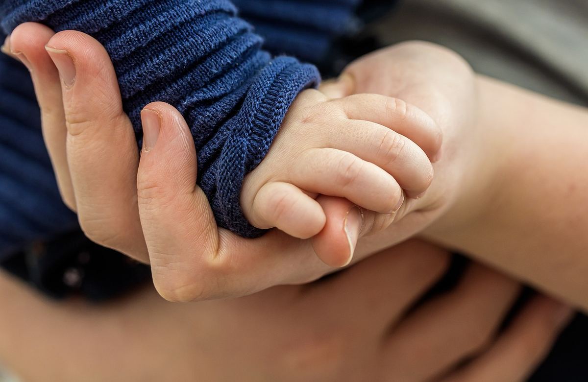 Une main adulte serre doucement la petite main d'un bébé Une main adulte serre doucement la petite main d'un bébé