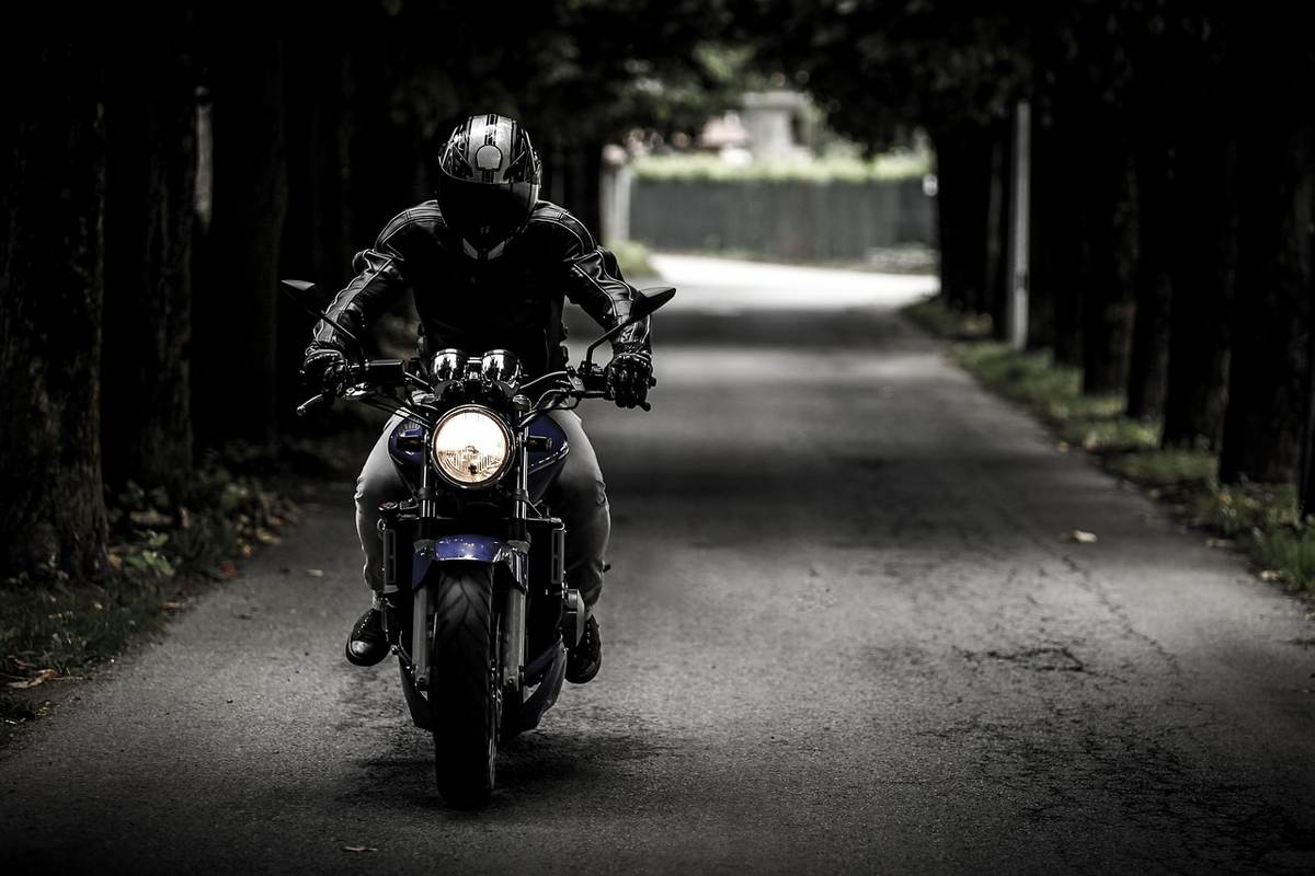 Un coureur en tenue noire conduit une moto sur une allée d'arbres Un coureur en tenue noire conduit une moto sur une allée d'arbres